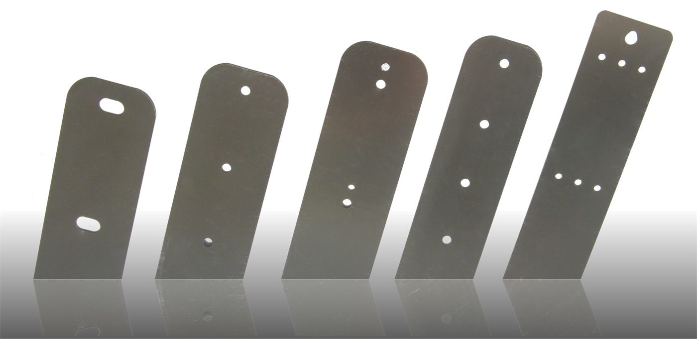 Five steel conveyor belt plates of different lengths and hole patterns, stood upright side by side on a reflective surface